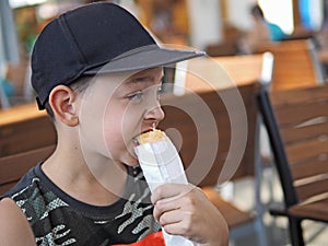 Young boy eats a hot dog at outdoor restaurant