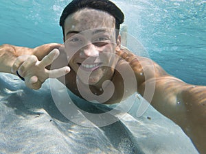 Young boy enjoy summer holiday vacation taking selfie underwater swimming at the sea with sand ground and blue water. Happy