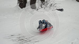 Young boy enjoying the thrill of sliding down a snow-covered hill on his plastic sleds and falling on ice.