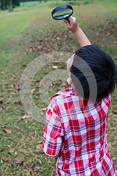 Young boy exploring nature with magnifying glass. Outdoors.