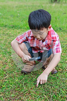 Young boy exploring nature with magnifying glass. Outdoors in th