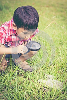 Young boy exploring nature with magnifying glass. Outdoors in th