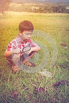 Young boy exploring nature with magnifying glass. Outdoors in th