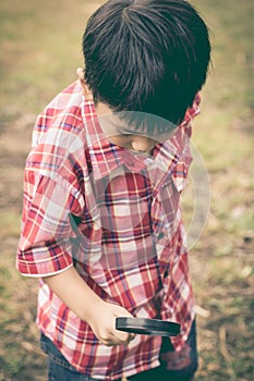 Young boy exploring nature with magnifying glass. Outdoors. Vintage style.