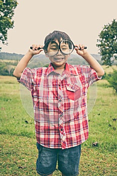 Young boy exploring nature with magnifying glass. Outdoors. Vintage style.
