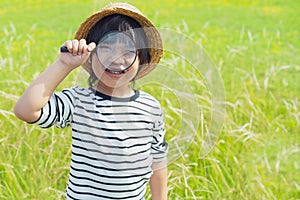 Young boy exploring nature in the meadow with a magnifying glass looking at flowers. Curious children in the woods