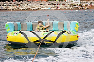 Young boy exudes joy while riding an inflatable tube towed by a boat in the ocean. Happy school child having fun in