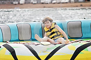 Young boy exudes joy while riding an inflatable tube towed by a boat in the ocean. Happy school child having fun in