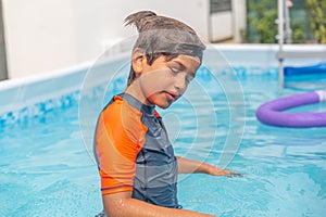 Young boy with eyes closed enjoying a moment in the pool, sun-kissed water sparkling around him