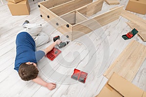 A young boy falls asleep on the floor while assembling furniture.