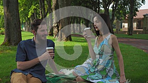 A young boy and girl held a meeting and picnic in the park. They talk and drink coffee while sitting on the lawn. Smile