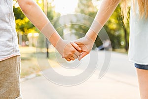 Young boy and girl hold hands and stroll in the park in sunny we