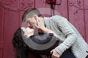 Young boy and girl are hugging and kissing with closed eyes. Loving couple on a red wooden wall background