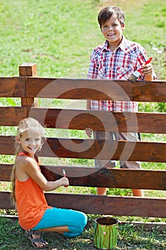 Young boy and girl painting a wooden fence