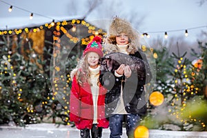 Young boy and girl posing on an ice rink with black little pig. Snowing.