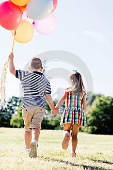 Young boy and a girl running with a bunch of colorful balloons.