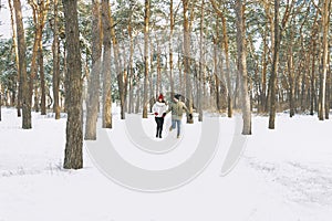 Young boy and girl running in winter park. Young couple are running on sunny day in snowy forest