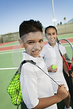 Young boy and girl with tennis equipment on tennis court focus on boy portrait photo