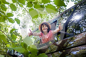 A young boy is giving thumbs up from the window of a car