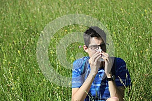 Young boy with glasses blowing his nose because of allergy in th