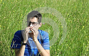 Young boy with glasses blowing his nose because of allergy in th