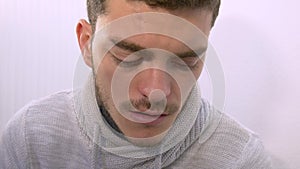 Young boy with glasses coughs and takes off his glasses to rub his eyes. Man wears a turtleneck sweater on a white background.