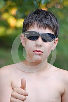 Young boy in the glasses from the sun resting in nature and showing the class with a thumb of his hand. He loves to relax with his
