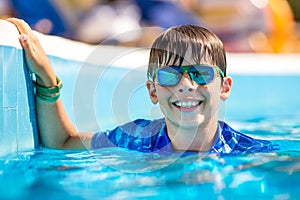 Young boy in googles holding edge of swimming pool. Enjoying time in the refreshing water