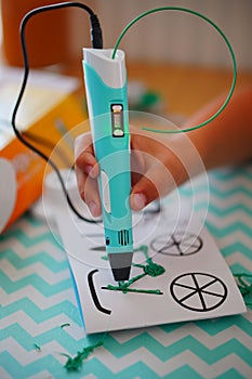 Young boy happily drawing a picture of a bicycle with a 3D drawing pen on a white sheet of paper