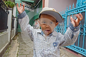 a young boy with a hat on is standing in front of a fence