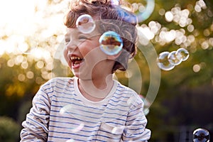 Young Boy Having Fun In Garden Chasing And Bursting Bubbles