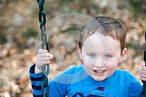Young boy having fun outside at park on a playground swing set