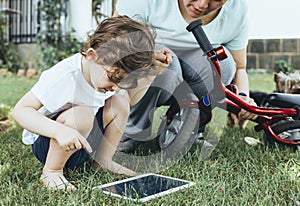 A young boy with his mother sitting on the grass in a park using a tablet PC