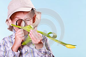 Young boy hold flower and magnifying glass.