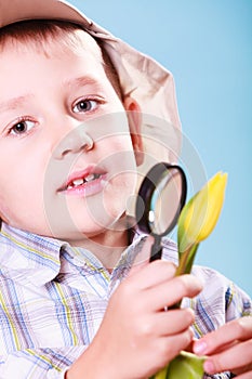 Young boy hold flower and magnifying glass.