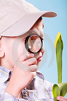 Young boy hold flower and magnifying glass.