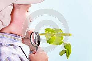 Young boy hold flower and magnifying glass.