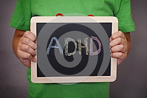 Young boy holds ADHD text written on blackboard