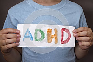 Young boy holds ADHD text written on sheet of paper