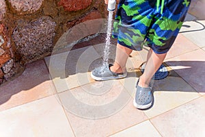 Young boy hosing the sand off himself and his shoe