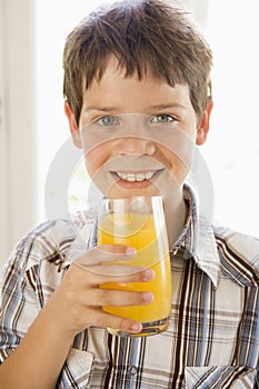 Young boy indoors drinking orange juice smiling