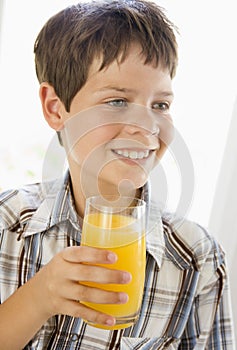 Young boy indoors drinking orange juice smiling