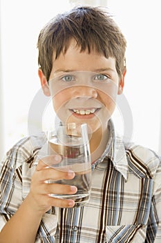 Young boy indoors drinking water smiling