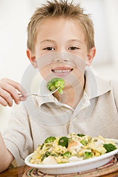 Young boy indoors eating pasta with brocolli