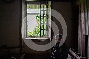 A young boy inside a room in an old crumbling house with an open window. The concept of poverty, homelessness