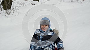 Young boy joyfully sledging down a snowy hill on his plastic sled. The snowy landscape, winter holidays and outdoor activities.