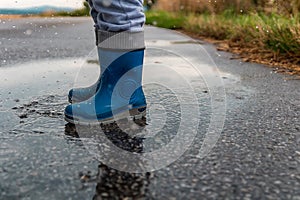 Young boy jump into puddle with gumboots and splash water on street