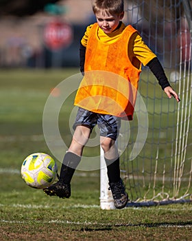 Young boy kicking soccer ball playing goalie in action shot during game