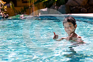 Young boy kid child eight years old having fun in swimming pool leisure activity thumbs up