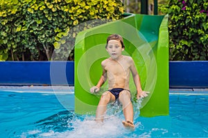 Young boy or kid has fun splashing into pool after going down water slide during summer